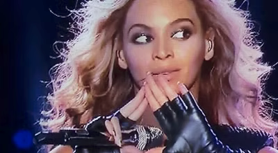 Close-up of Beyoncé on stage wearing a leather glove, with her hand raised near her face